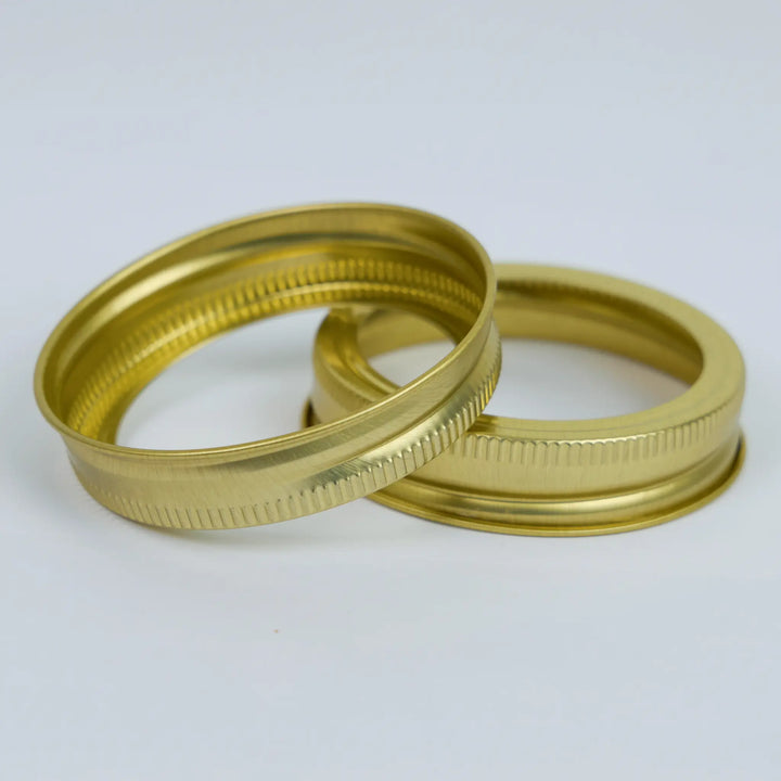 Two gold metal screw top canning bands made in usa on a white background