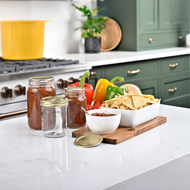 Kitchen counter with jars of food, a bowl of chips, and vegetables on a cutting board Assorted sizes of Superb canning jars Canning jar with airtight lid High-quality canning jars for food storage Sunlit countertop with filled canning jars Regular mouth jars filled with homemade salsa