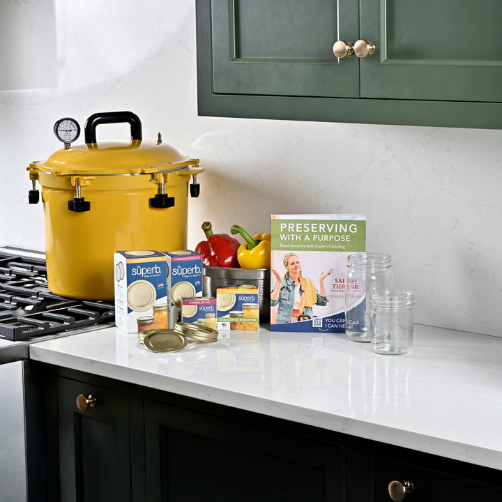 Canning supplies including jars, boxes, and the Preserving with a Purpose book on a kitchen counter Regular mouth pint canning jar set on kitchen counter Wide mouth quart canning jar set on kitchen counter Regular mouth canning jar with airtight lid High-quality canning jars for food storage Preserving with a Purpose book by Sarah Thrush High-performance yellow pressure canner